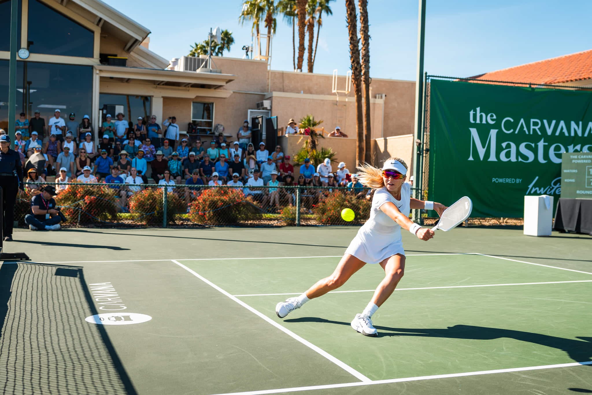 Pickleball pro stretching wide for a backhand in front of a packed crowd at the Carvana Masters.